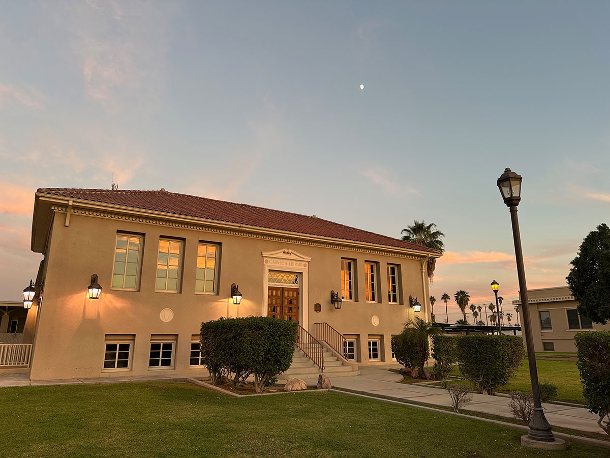 Calexico_CA_Carnegie---Mara-Cota A stucco library at sunset. Hedges and a lampost are visible.