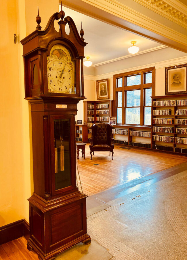 A brown antique grandfather clock in a library