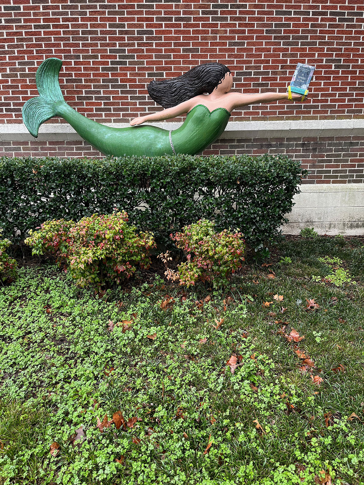 A mermaid statue outside of a brick library.