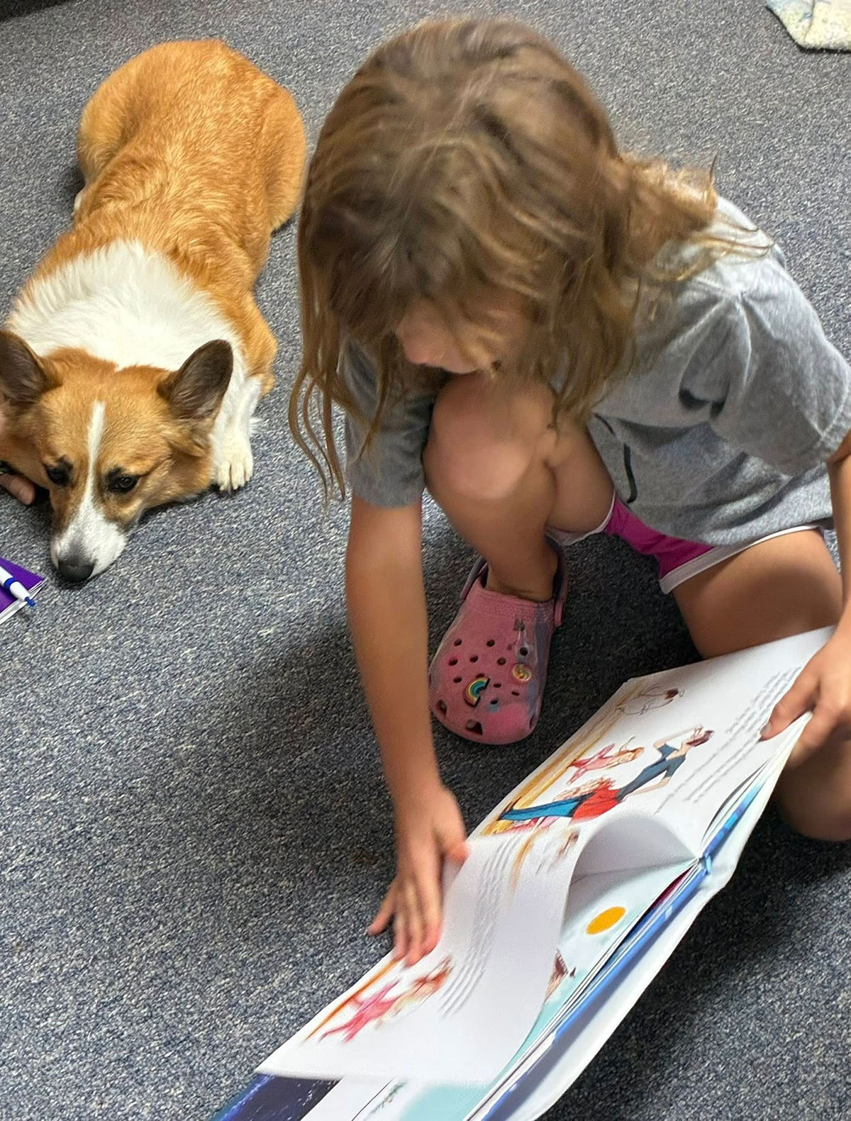 A girl reads a picture book next to a dog