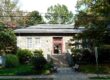 A rectangular stone library with red trimmed door and trees and shrubs around it.