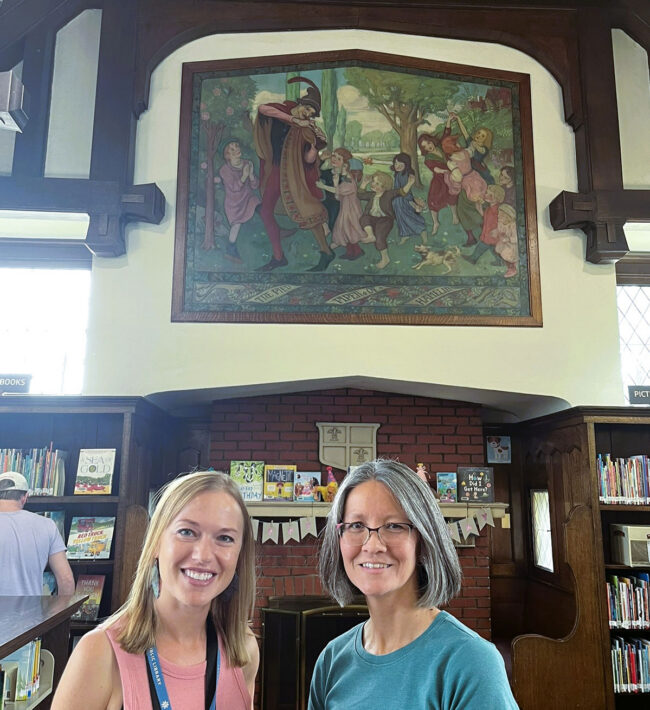 Two women stand in front of a large painting.