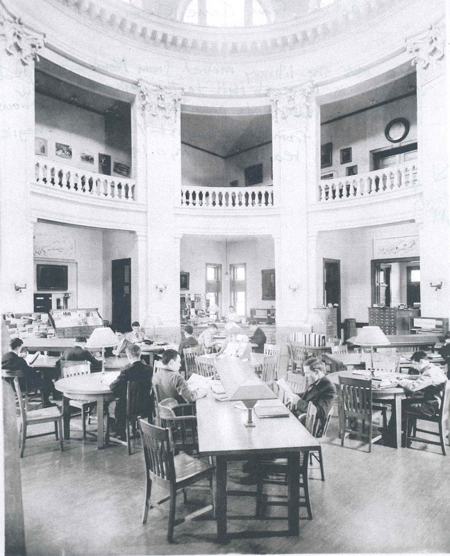 Black and white photo of a library interior with reading tables and high domed ceiling.
