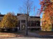 A red brick library with white trim behind trees with fall colors.