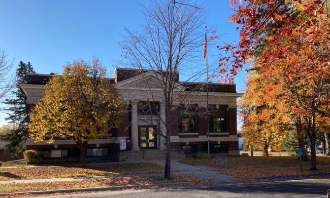 A red brick library with white trim behind trees with fall colors.