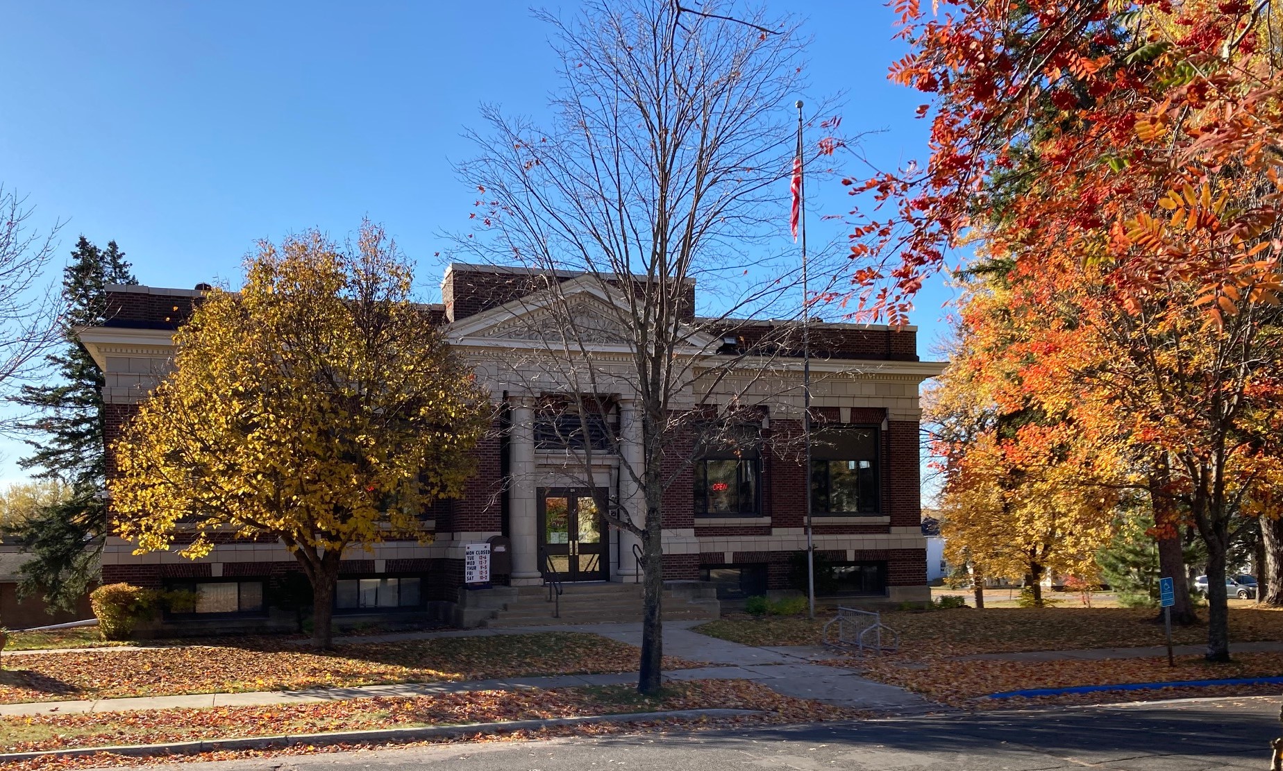 A red brick library with white trim behind trees with fall colors.