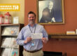 A man stands before a photo of Andrew Carnegie holding a check.