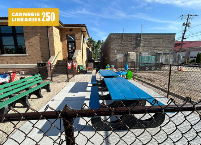 Colored wooden tables in a concrete yard behind a library