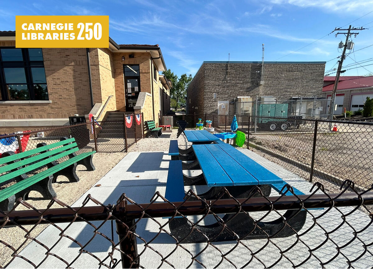 Colored wooden tables in a concrete yard behind a library
